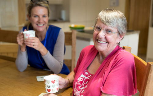 Volunteer and elderly woman drinking coffee and smiling.